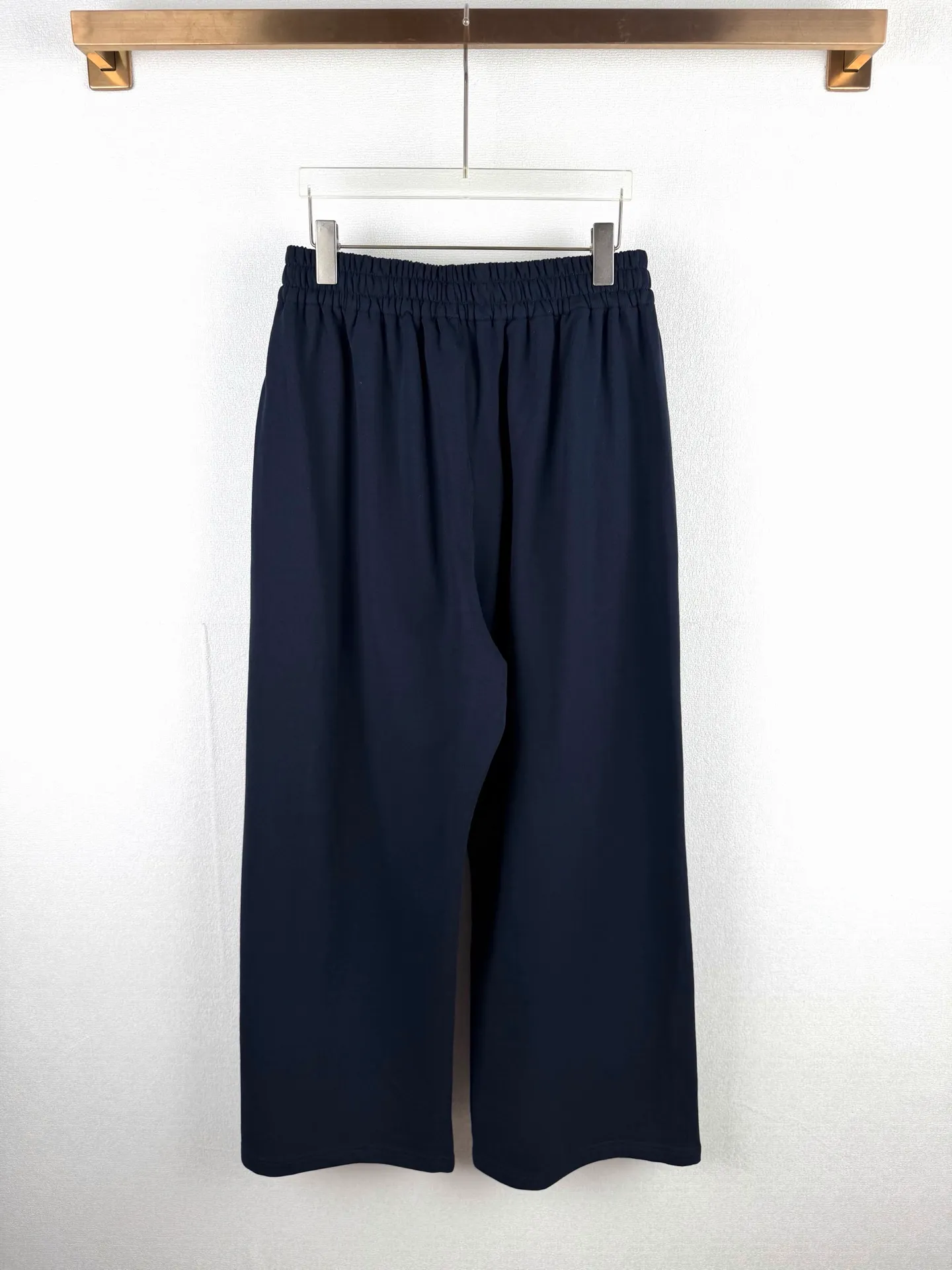 ACNE STUDIOS embroidered logo fleece sweatpants wide-leg trousers. Fabric: 32-count double yarn top + 16-count terry bottom yarn G The veil is made of 32-count fine yarn. The high-count yarn is smooth and delicate. After weaving, it forms a smooth and compact surface. It not only resists pilling and wear-resistant, but also gives the fabric a touch as delicate as skin. The base yarn is made of 16-count roving. The low-count yarn is fluffy and hairy. It naturally forms a rich terry layer during the weaving process, providing a sufficient source of fiber for subsequent sanding. This combination of fine surfaces and thick soles strikes a perfect balance between warmth and skin-friendliness. Mechanical sanding is the soul process of this fabric. By rubbing the bottom surface of the roller wrapped with emery leather at high speed, the fiber ends of the 16-count roving are evenly pulled out and cut off, forming a dense and uniform short pile layer. The smoothness and neatness of needle embroidery and the soft velvet feel of brushed fabrics form a material dialogue between hardness and softness. The embroidery area is smooth and crisp, with sharp lines, like delicate inscriptions carved on a rich suede canvas; while the surrounding brushed fabric presents a soft matte natural texture. The spacing between stitches is consistent and the strength is balanced to ensure that each stitch is placed accurately. This rigorous stitching structure makes the edges of the logo present a sharp and clear outline, and the strokes of the text are full and smooth. Even the curved turning points of the floral fonts can achieve a smooth transition through the connection of tight stitches.